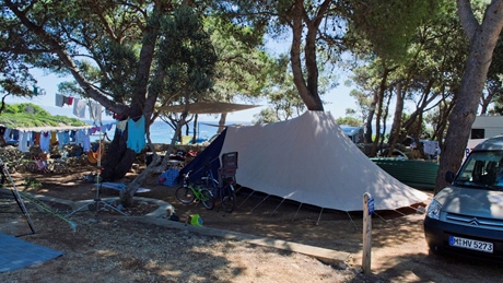 Een camping met een grote witte tent tussen de bomen, fietsen en een nabijgelegen busje