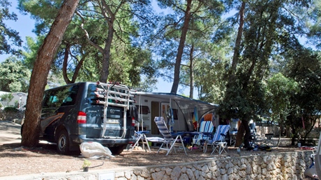Een camper en kampeeropstelling in een bosrijk gebied met verschillende stoelen en een tafel