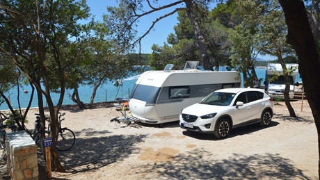 Een witte SUV geparkeerd naast een caravan op een schilderachtige camping aan een meer, omringd door bomen