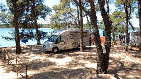 Camper geparkeerd op een schilderachtige camping aan het meer omgeven door bomen