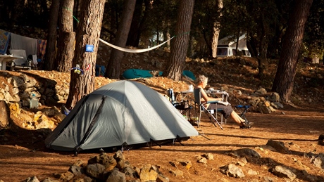 Iemand ontspant in een campingstoel naast een tent in een bosrijke omgeving