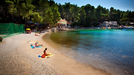 A serene beach scene at Bokinic with people sunbathing and calm waters reflecting the blue sky