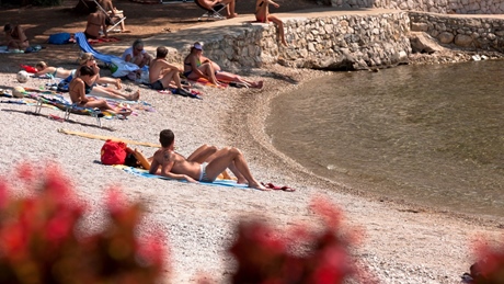 People relaxing on a pebbled beach at Bokinic, with towels and a stone wall nearby
