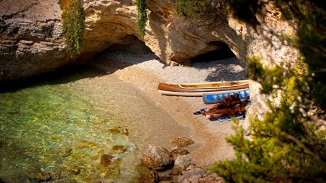 Beach with kayaks and sunbathers by a rocky cave