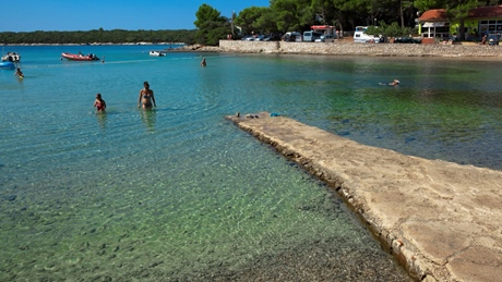 People enjoying a sunny day at a picturesque beach with calm waters and a stone pier