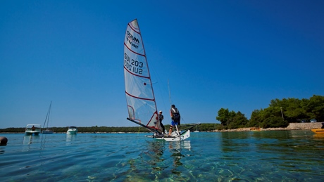 Two people sailing a boat on clear blue water under a sunny sky