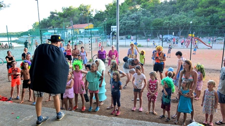 A group of children gathered outdoors for a performance led by a person in costume