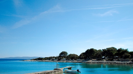 Scenic view of a small boat docked by the clear blue waters and a tree-lined shore on a sunny day