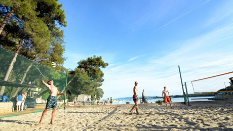 People playing beach volleyball on a sandy court by the sea