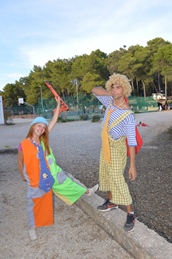 Two children dressed in colorful clown costumes posing outside