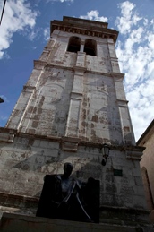 Historical stone tower with a statue in the foreground under a blue sky with clouds