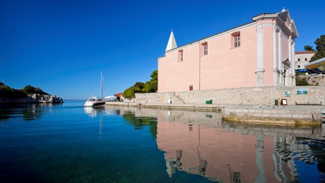 A scenic view of a pink church by the waterfront in Losinj