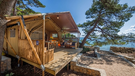 A cozy glamping tent with a wooden deck overlooking the sea, surrounded by pine trees
