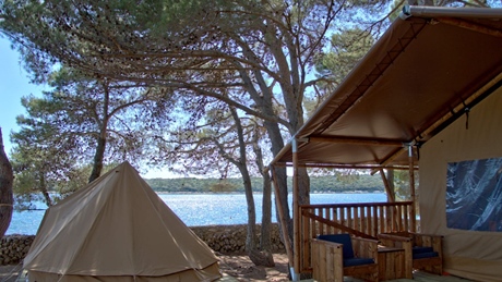 A glamping tent and seating area under trees by the sea
