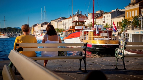 A scenic view of Mali Losinj's harbor with people sitting on a bench