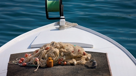 A fishing net with floats on the deck of a white boat, floating on calm blue water