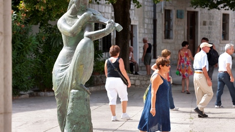 A bronze statue of a woman playing a violin with people walking nearby