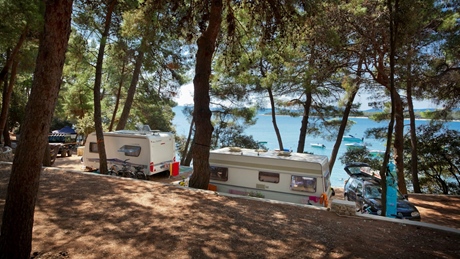 Two caravans parked in a scenic forested area near the sea