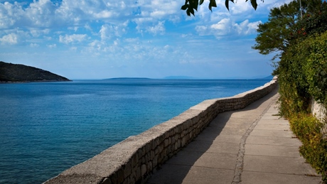 Coastal walkway alongside a blue sea under a partly cloudy sky