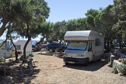 A camper van parked among trees at a campsite with bicycles nearby