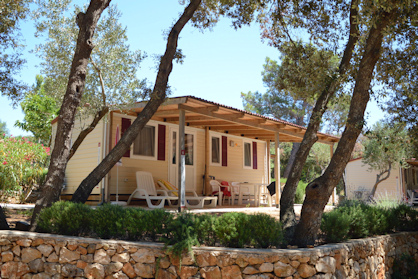 A cozy mobile home with a shaded porch surrounded by trees