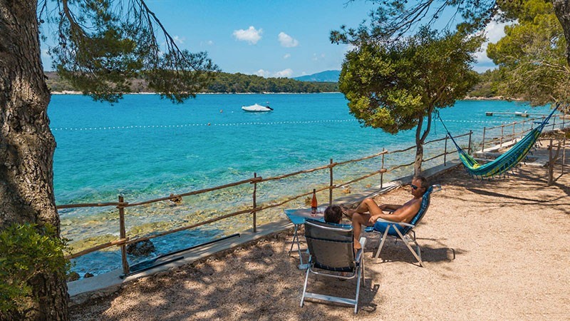 Two people relaxing by the sea with a hammock and a boat in the background