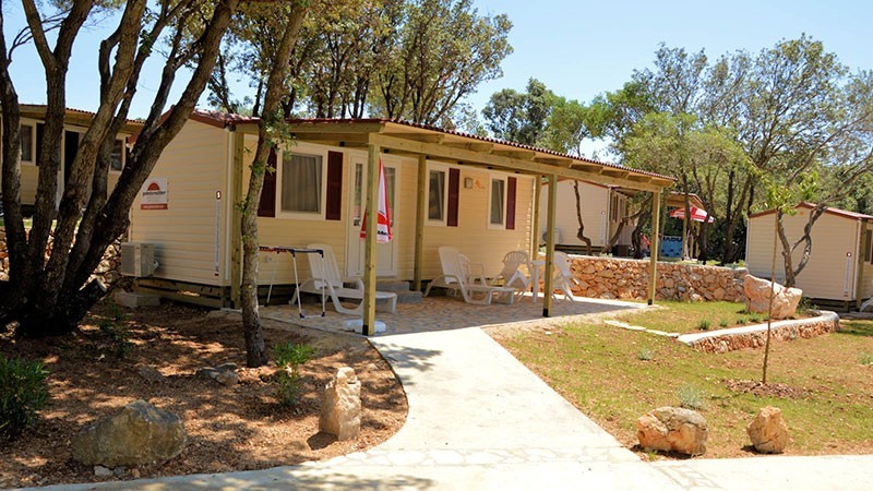 A cozy mobile home situated in a wooded area with a small patio and chairs
