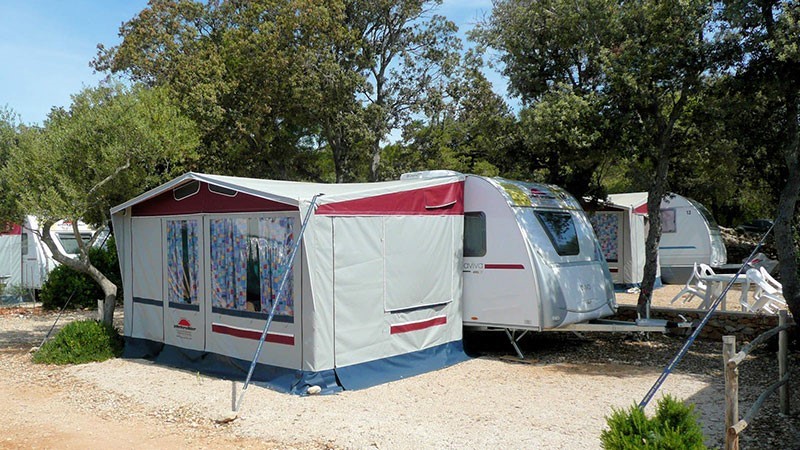 A campsite featuring an Adria caravan with an attached awning, set among trees