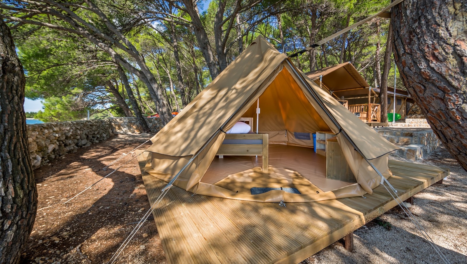Ein Baldarin-Campingzelt unter Kiefern, mit einem komfortablen Innenraum und Holzboden