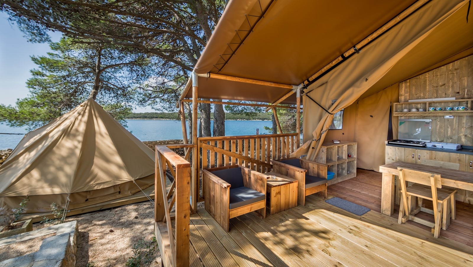 Outdoor glamping setup at Baldarin with wooden deck, tent, and seating area near the sea