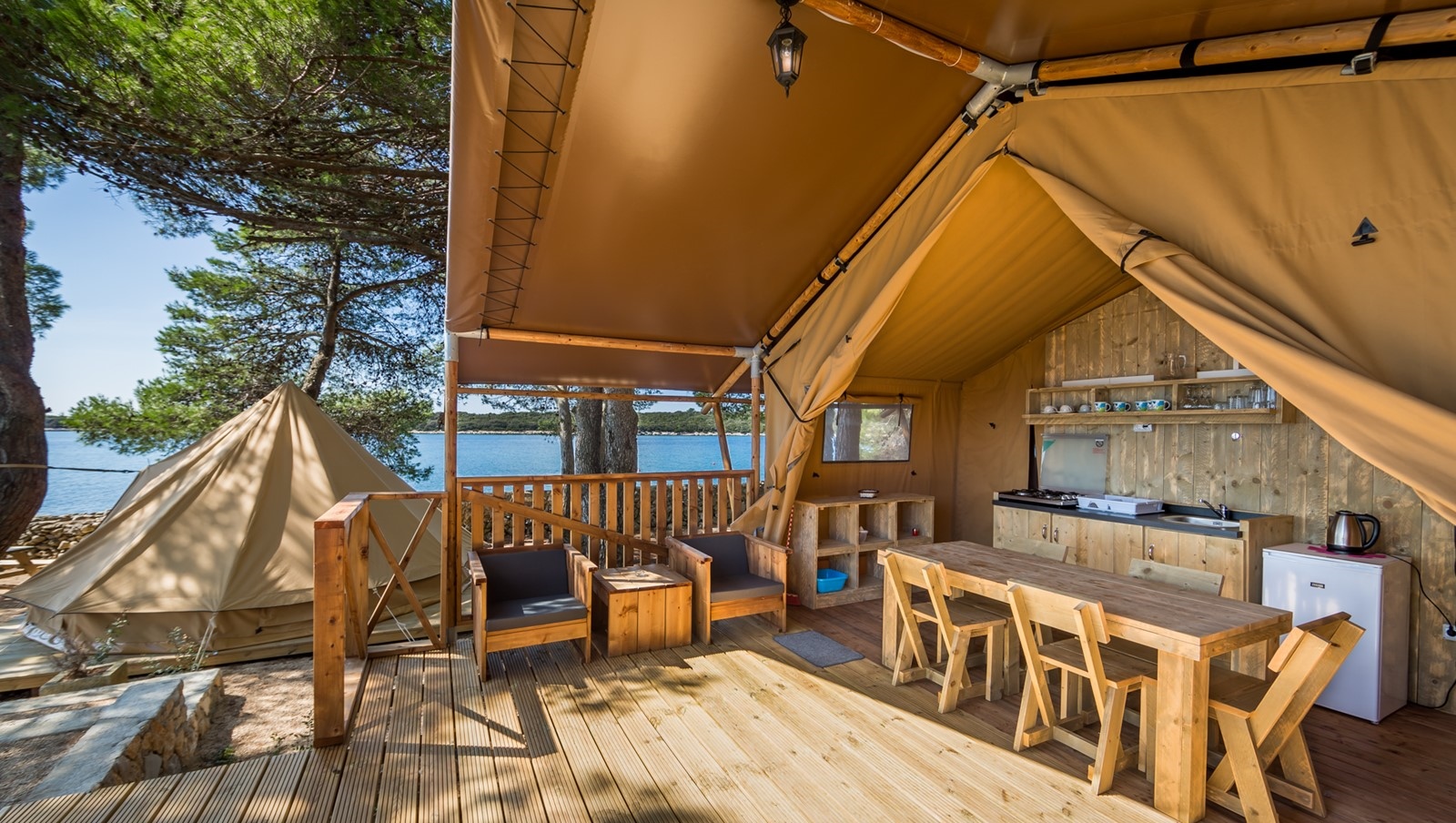 Outdoor glamping setup at Baldarin with wooden deck, tent, and seating area near the sea