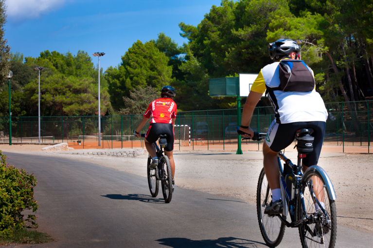 Two cyclists riding on a paved path surrounded by trees