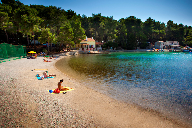 A serene beach scene with people relaxing on the sand near a small bay surrounded by pine trees